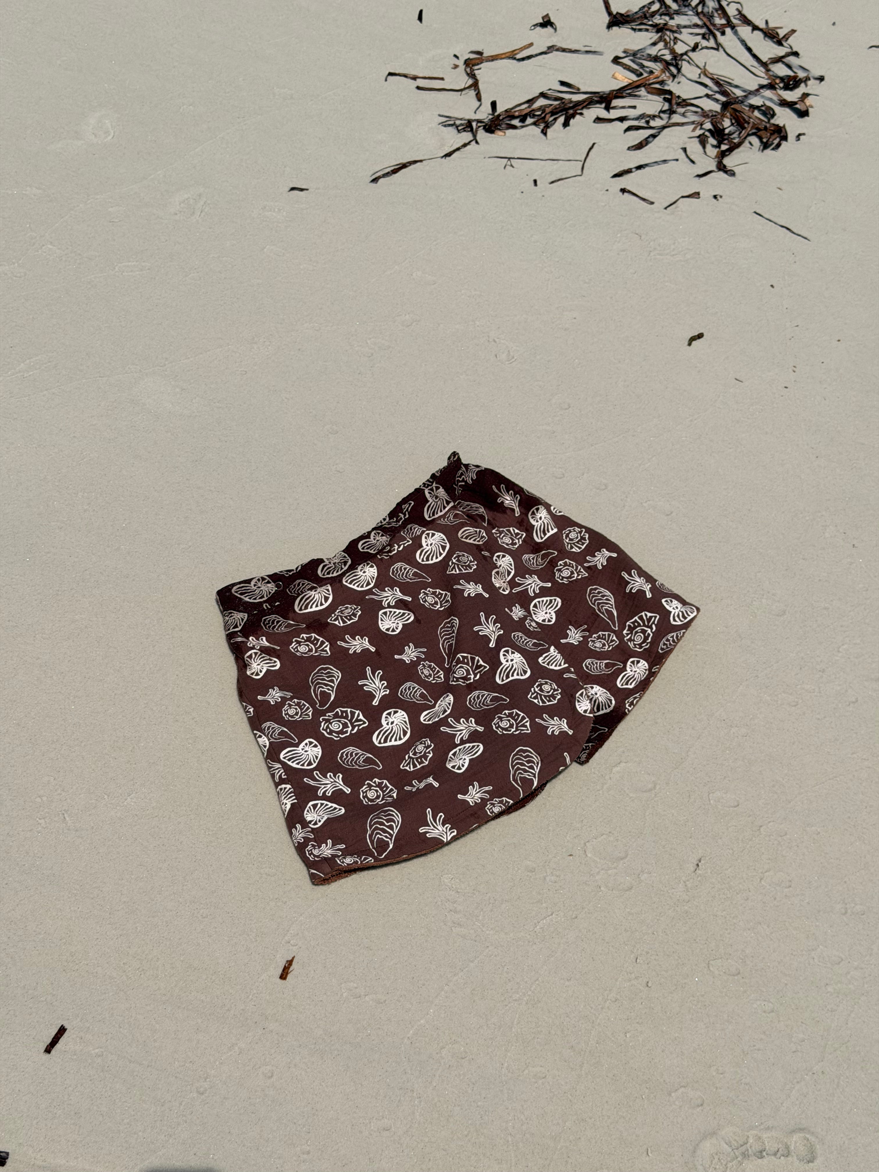 Brown fabric with white shell patterns in the shape of a Skort for women to wear over their swimwear that is made from Terry towelling on a sandy surface